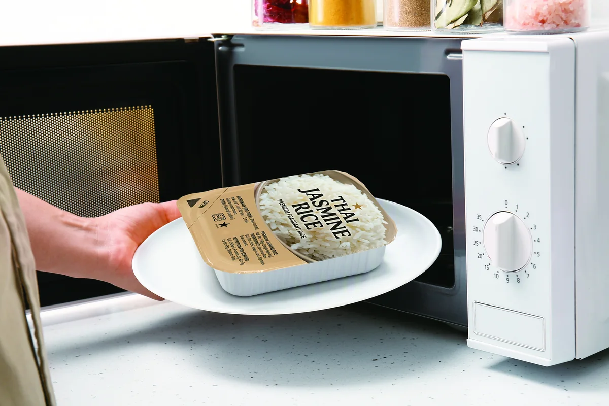 Hand placing a cooked-rice pack on a plate into a microwave oven
