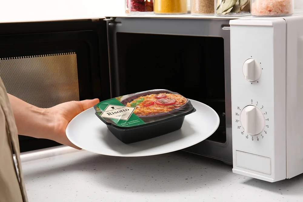 Hand placing a ready-meal tray on a plate into a microwave oven