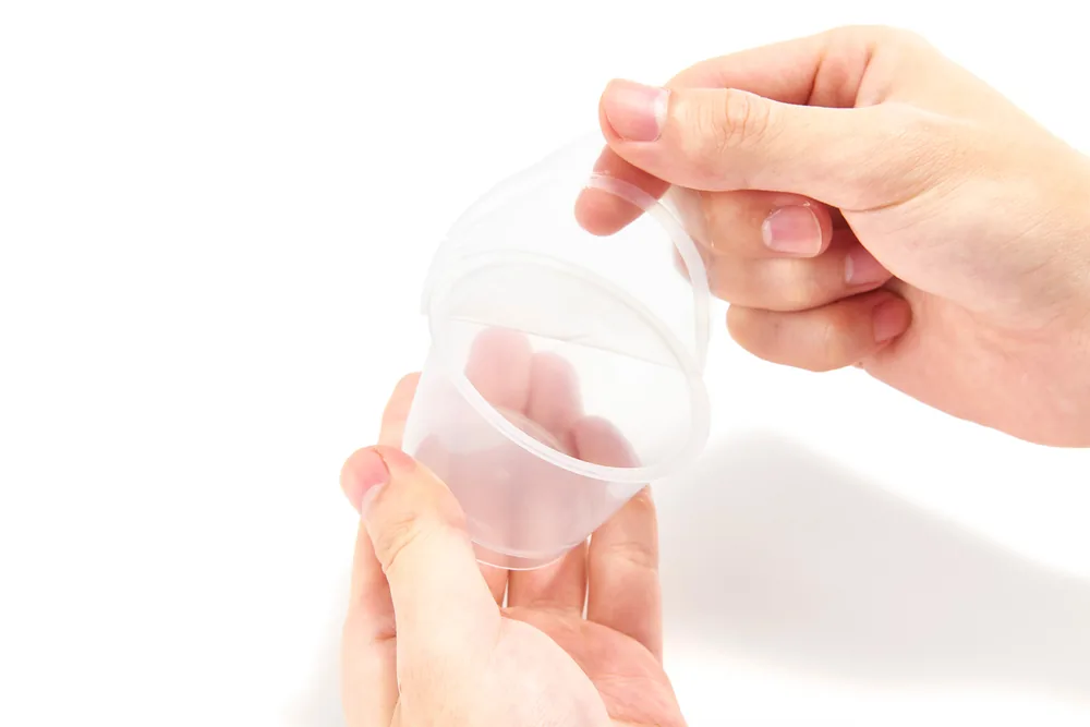 Hand peeling the lid film off a plastic cup