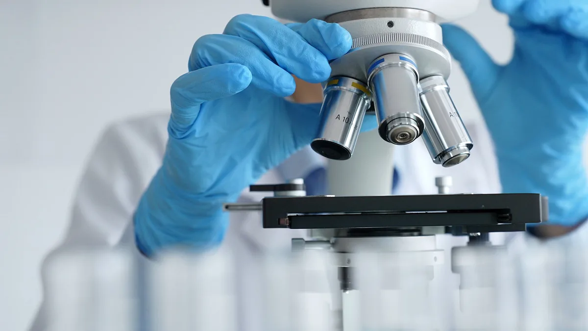 Researcher in blue gloves examining a sample under a microscope